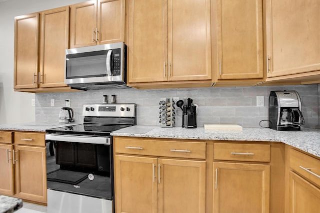 kitchen with tasteful backsplash, appliances with stainless steel finishes, and light stone counters