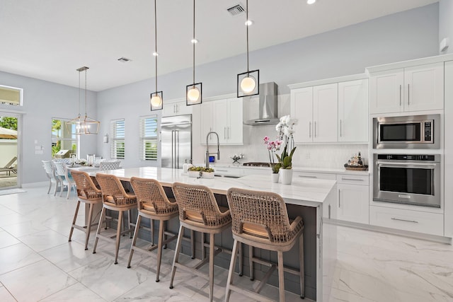 kitchen with visible vents, backsplash, wall chimney range hood, built in appliances, and marble finish floor