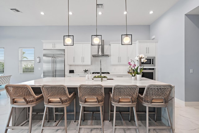 kitchen with tasteful backsplash, wall chimney range hood, built in appliances, a large island with sink, and marble finish floor