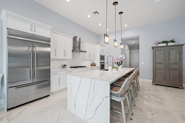 kitchen with wall chimney range hood, built in appliances, decorative backsplash, marble finish floor, and white cabinetry