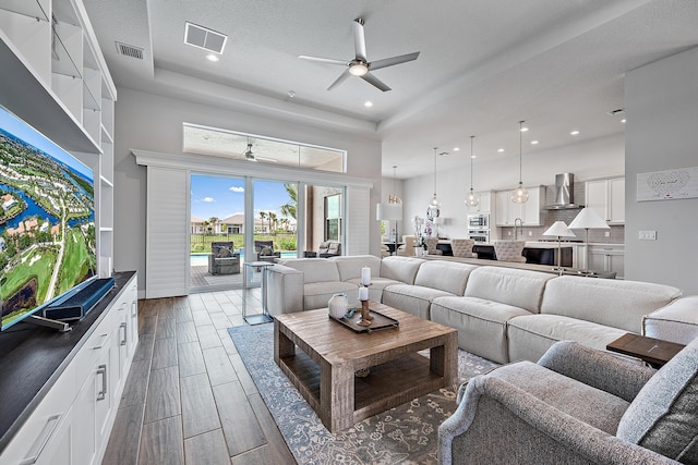 living area with a raised ceiling, a high ceiling, visible vents, and wood finish floors