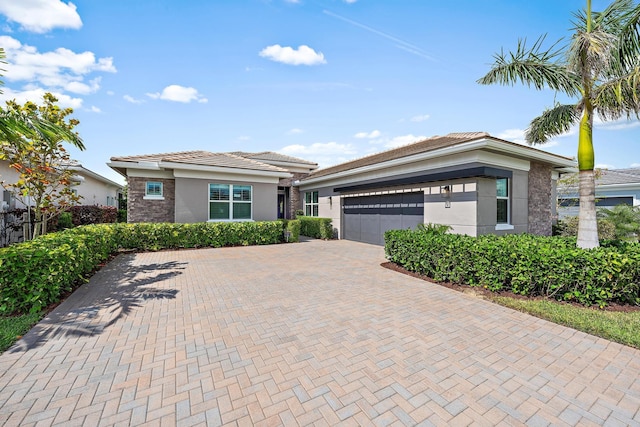 prairie-style home with a tiled roof, stucco siding, an attached garage, and decorative driveway