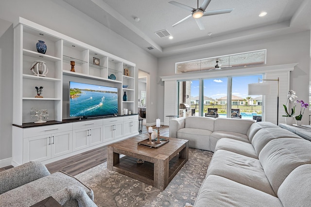 living area featuring visible vents, a ceiling fan, a tray ceiling, wood finished floors, and baseboards