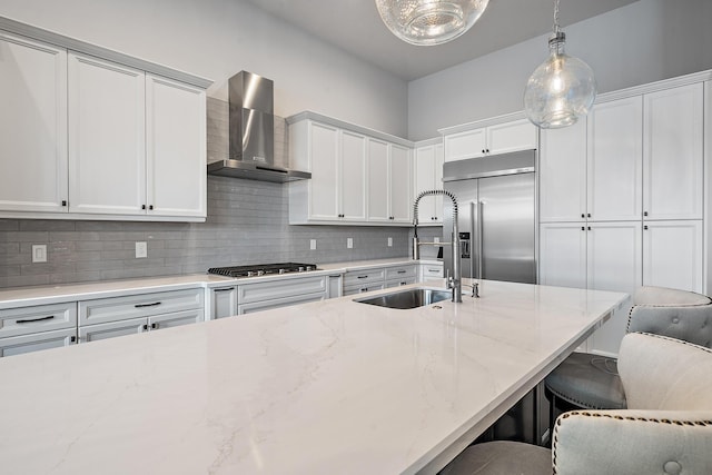 kitchen featuring wall chimney range hood, stainless steel built in refrigerator, decorative light fixtures, a breakfast bar area, and white cabinets