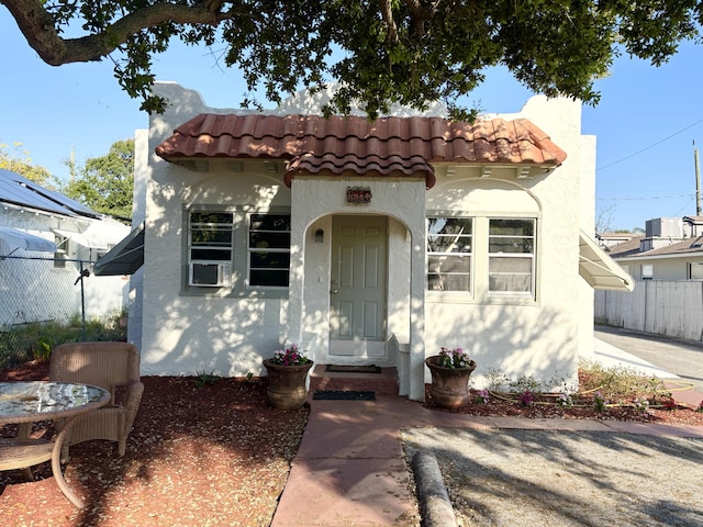 mediterranean / spanish-style house with a tile roof, fence, and stucco siding