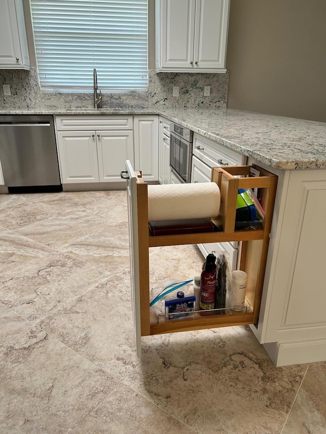 kitchen with light stone counters, stainless steel appliances, backsplash, white cabinetry, and a sink