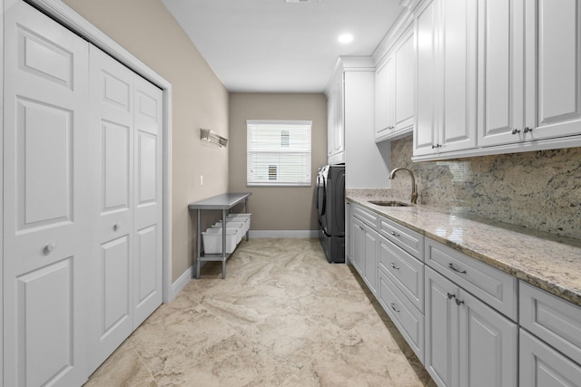 washroom featuring cabinet space, a sink, baseboards, and washing machine and clothes dryer