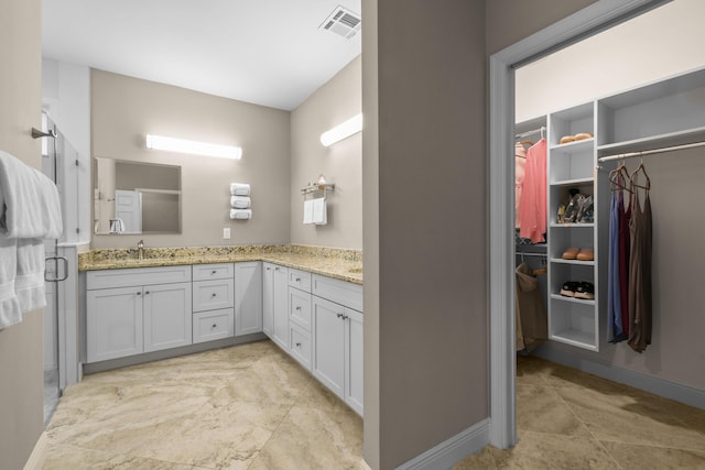 bathroom featuring visible vents, baseboards, a walk in closet, vanity, and a shower stall