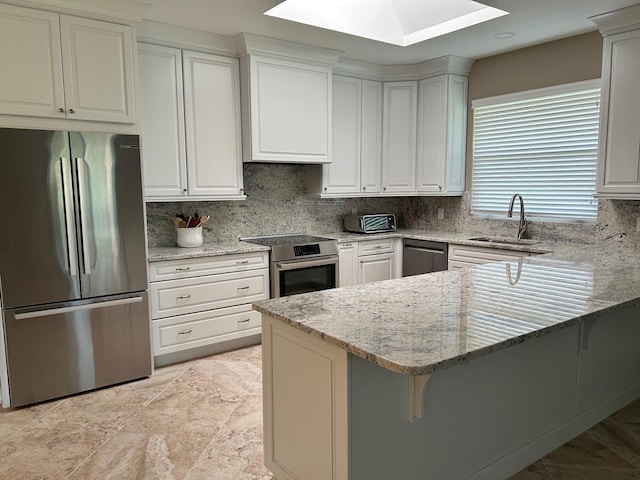 kitchen with a peninsula, light stone counters, stainless steel appliances, and a sink