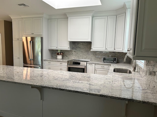 kitchen featuring visible vents, white cabinets, light stone countertops, stainless steel appliances, and a sink