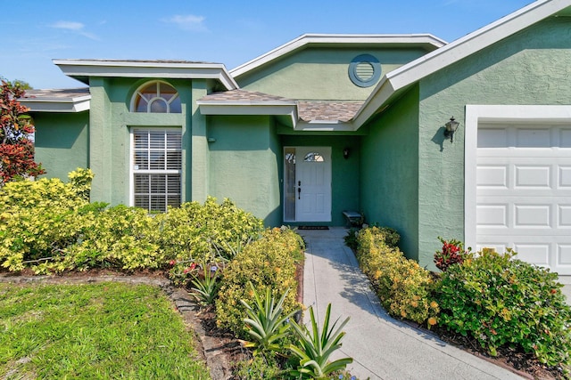 entrance to property featuring an attached garage, roof with shingles, and stucco siding