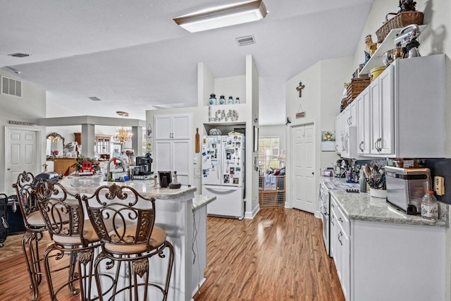 kitchen with light wood-type flooring, white appliances, visible vents, and a kitchen breakfast bar