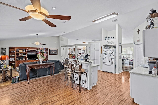 kitchen featuring light stone counters, lofted ceiling, visible vents, light wood-style flooring, and freestanding refrigerator