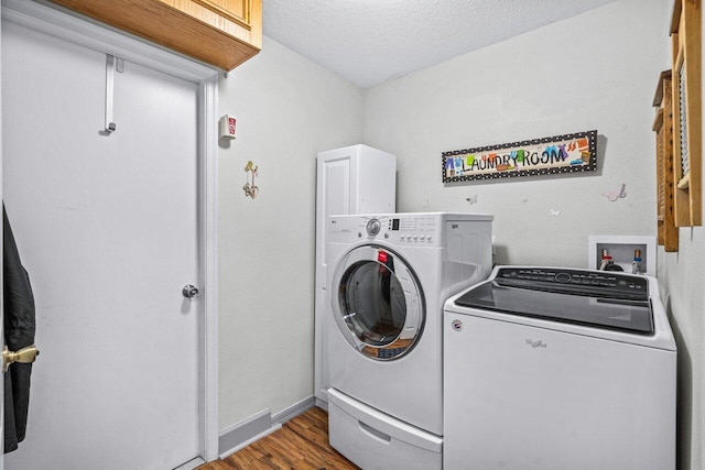 clothes washing area with a textured ceiling, laundry area, wood finished floors, baseboards, and washer and clothes dryer