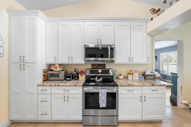 kitchen with lofted ceiling, light tile patterned flooring, white cabinetry, appliances with stainless steel finishes, and light stone countertops