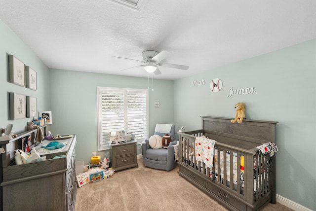 carpeted bedroom featuring a ceiling fan, a nursery area, a textured ceiling, and baseboards