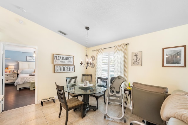 dining area with light tile patterned floors, ceiling fan with notable chandelier, visible vents, baseboards, and vaulted ceiling