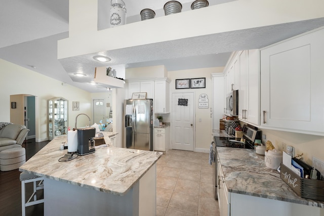 kitchen with a breakfast bar, stainless steel appliances, open floor plan, white cabinets, and light stone countertops