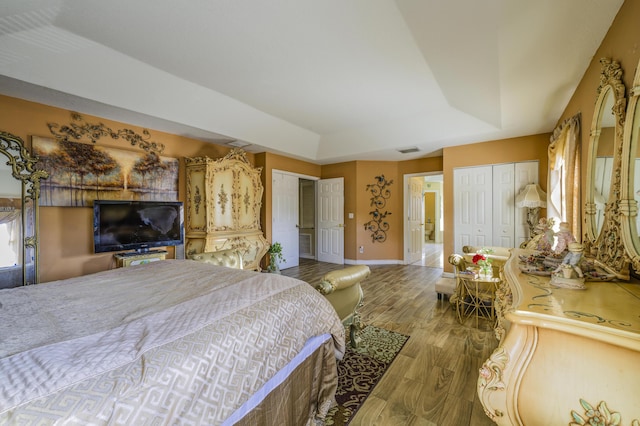 bedroom featuring wood finished floors, visible vents, multiple closets, baseboards, and a tray ceiling