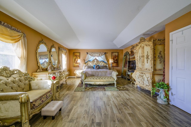 bedroom with a raised ceiling, wood finished floors, visible vents, and baseboards