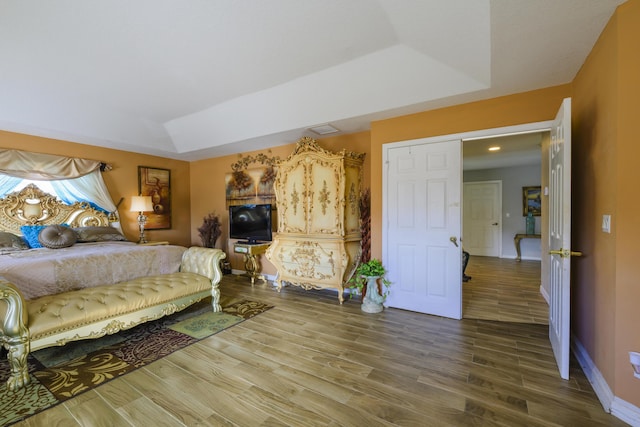 bedroom featuring a tray ceiling, visible vents, baseboards, and wood finished floors