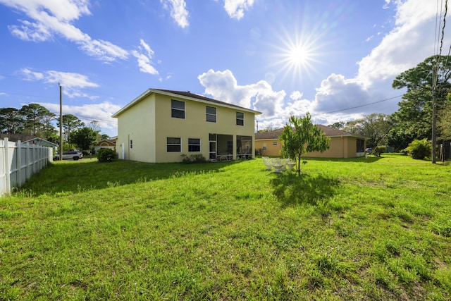 back of house featuring a lawn, fence, and stucco siding