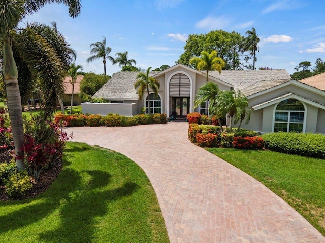 view of front of house with french doors, decorative driveway, a front yard, and stucco siding