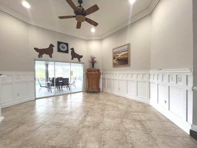 empty room featuring a wainscoted wall, ceiling fan, ornamental molding, and a decorative wall