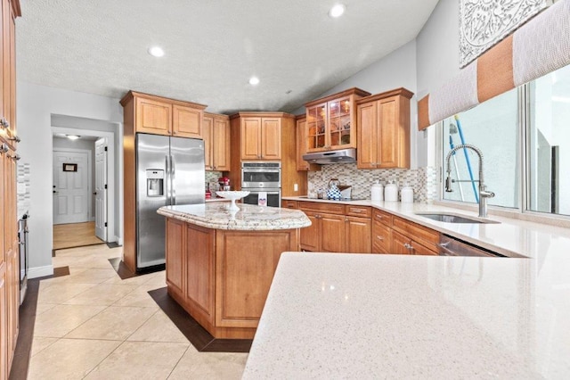 kitchen featuring light stone counters, stainless steel appliances, tasteful backsplash, a sink, and under cabinet range hood