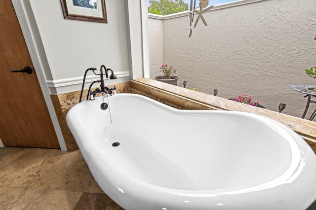 full bathroom with a freestanding tub and a textured wall