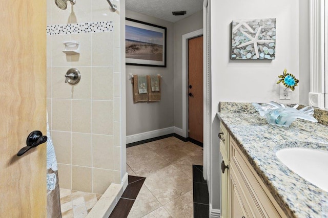 bathroom featuring baseboards, visible vents, tile patterned flooring, a tile shower, and vanity