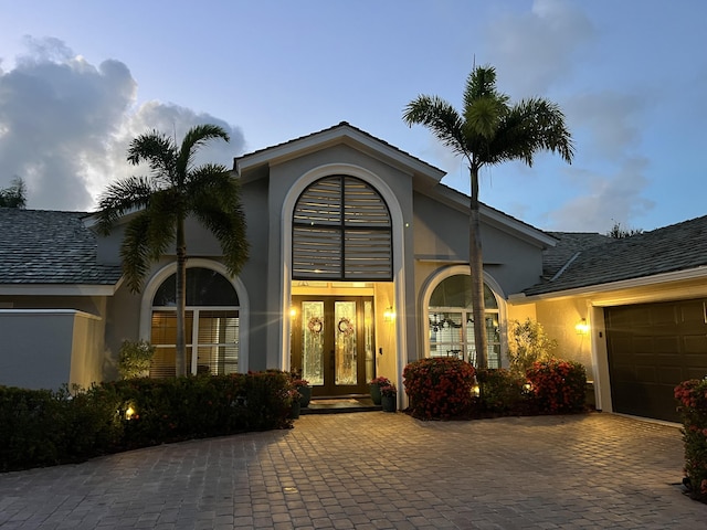 doorway to property featuring an attached garage, stucco siding, decorative driveway, and french doors