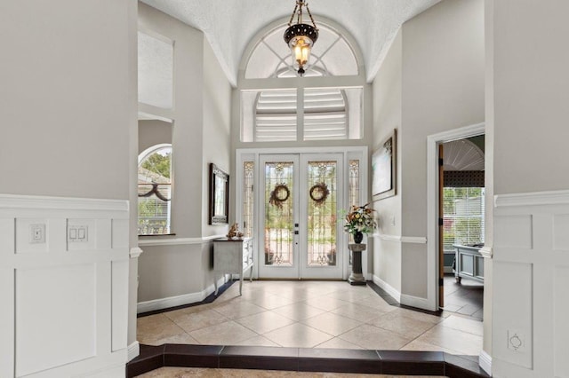 tiled entryway with french doors, baseboards, a decorative wall, and a high ceiling