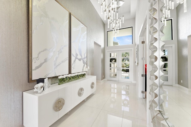 foyer entrance with french doors, a notable chandelier, a towering ceiling, light tile patterned flooring, and baseboards