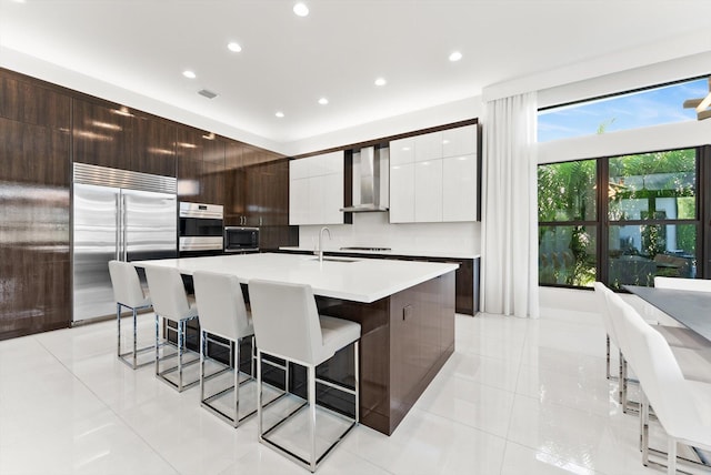 kitchen featuring a breakfast bar area, appliances with stainless steel finishes, a sink, wall chimney range hood, and modern cabinets