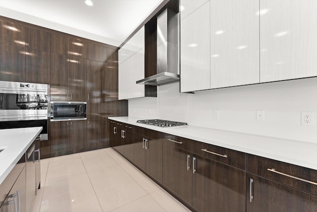 kitchen featuring dark brown cabinetry, wall chimney exhaust hood, modern cabinets, light countertops, and gas cooktop