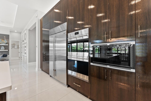 kitchen featuring light tile patterned flooring, dark brown cabinetry, baseboards, and built in appliances