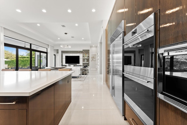 kitchen with modern cabinets, a tray ceiling, stainless steel appliances, light countertops, and light tile patterned flooring