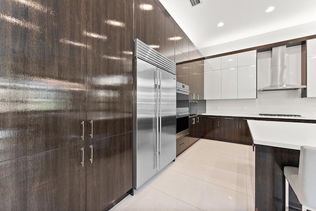 kitchen featuring modern cabinets, stainless steel appliances, light countertops, wall chimney range hood, and light tile patterned flooring