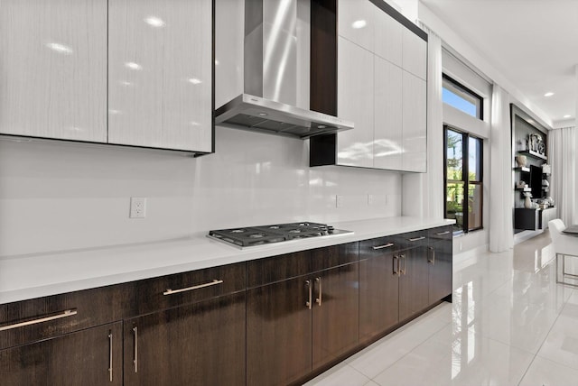 kitchen with dark brown cabinets, light countertops, backsplash, wall chimney exhaust hood, and stainless steel gas stovetop