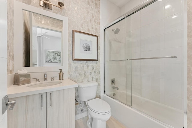 full bathroom featuring bath / shower combo with glass door, toilet, a ceiling fan, vanity, and wallpapered walls