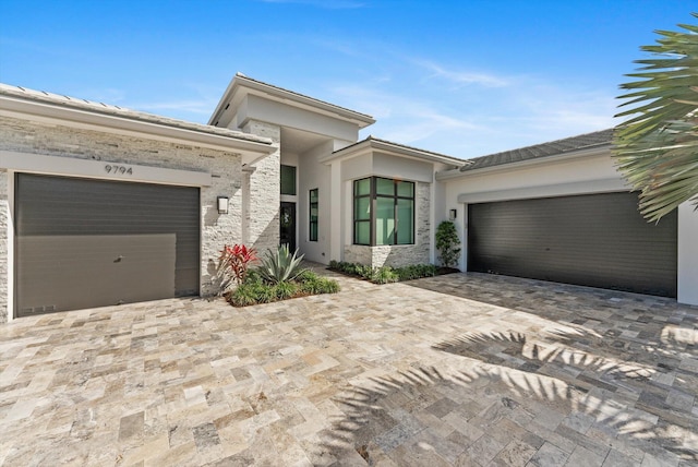 prairie-style home with stone siding, decorative driveway, an attached garage, and stucco siding