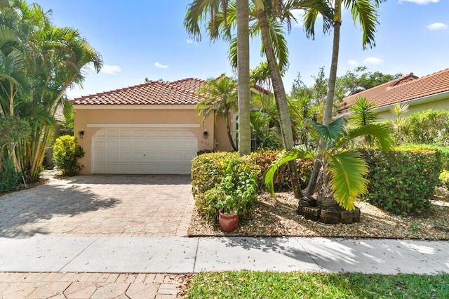 mediterranean / spanish home with a garage, decorative driveway, a tile roof, and stucco siding