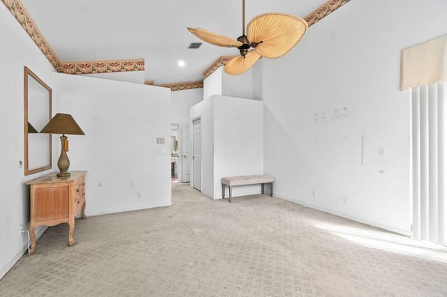 carpeted empty room with a ceiling fan, visible vents, and a towering ceiling