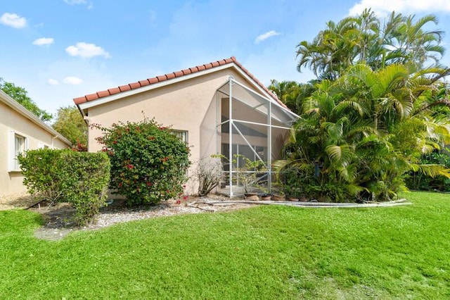 back of property featuring a tile roof, glass enclosure, a yard, and stucco siding