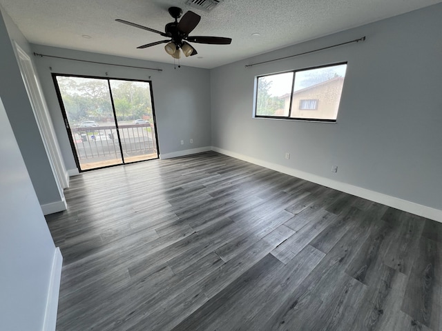 spare room featuring a wealth of natural light, a textured ceiling, baseboards, and dark wood-type flooring