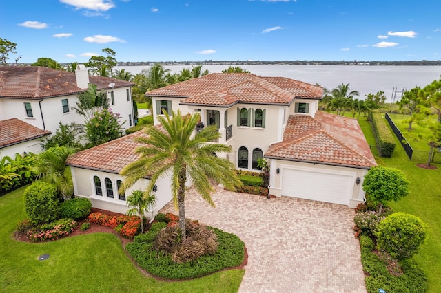 mediterranean / spanish-style home featuring a garage, a tile roof, decorative driveway, stucco siding, and a front lawn