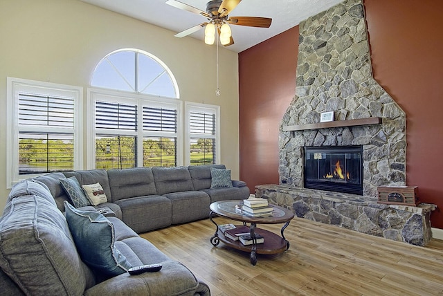 living room with a ceiling fan, a fireplace, a high ceiling, and wood finished floors