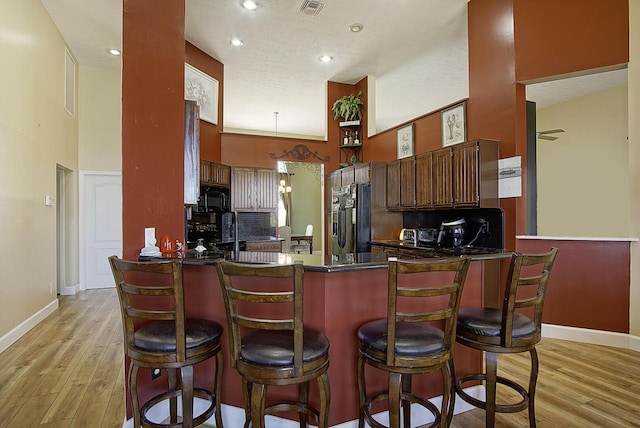 kitchen with dark countertops, a high ceiling, light wood-type flooring, a peninsula, and black appliances