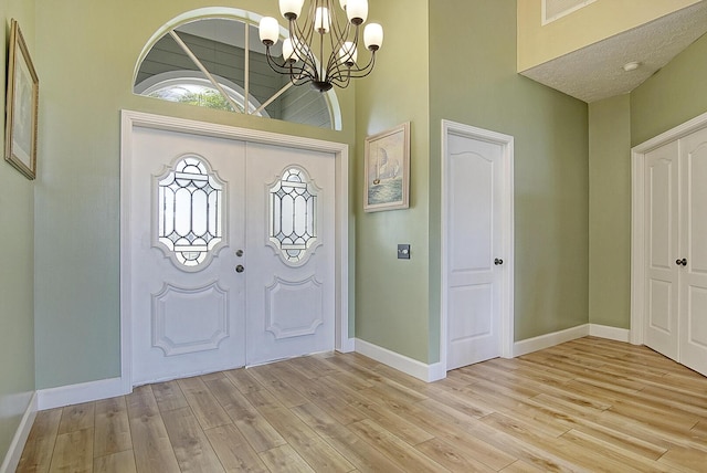 entrance foyer with visible vents, baseboards, a high ceiling, light wood-type flooring, and a notable chandelier